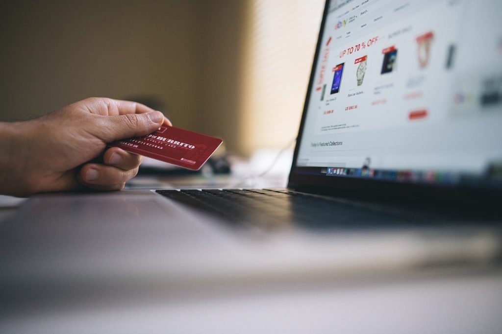 Person holding a credit card to the side of a laptop with products on the screen