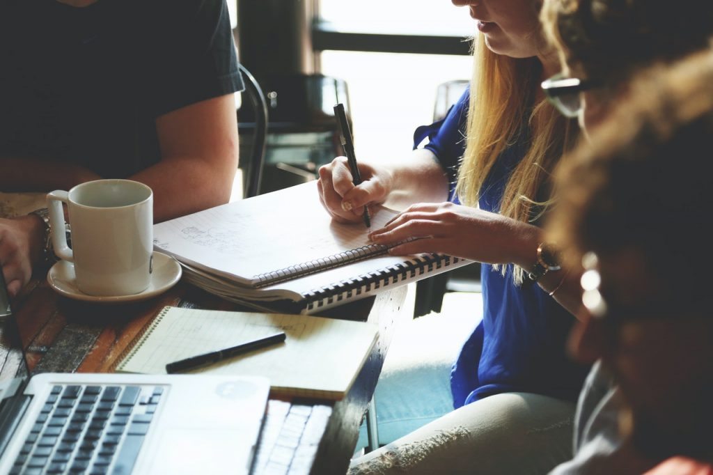 One person writing in a notebook surrounded by a team of people.